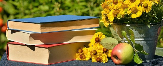a stack of books next to a vase of flowers and an apple