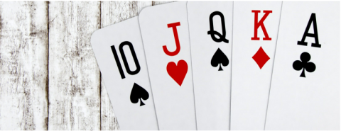 There is a wooden table with five playing cards fanned out. They are the 10 of spades, Jack of hearts, Queen of spades, King of diamonds, and Ace of clubs