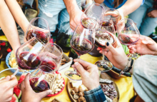 A group of people are clinking wine glasses as they sit down to a meal