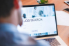 A blurred out person is starting at a laptop that has the words "JOB SEARCH" written across it